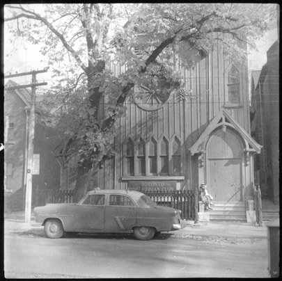 Vintage picture of the front of the Heliconian Club Hall. A car and tree stand out front.